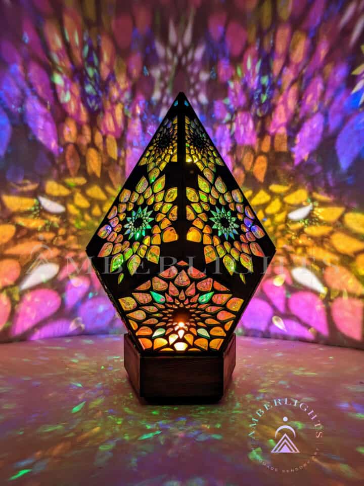 Handcrafted pyramid-shaped sensory lamp by AmberLights, adorned with intricate multicolored patterns casting vibrant kaleidoscopic projections onto surrounding surfaces.
