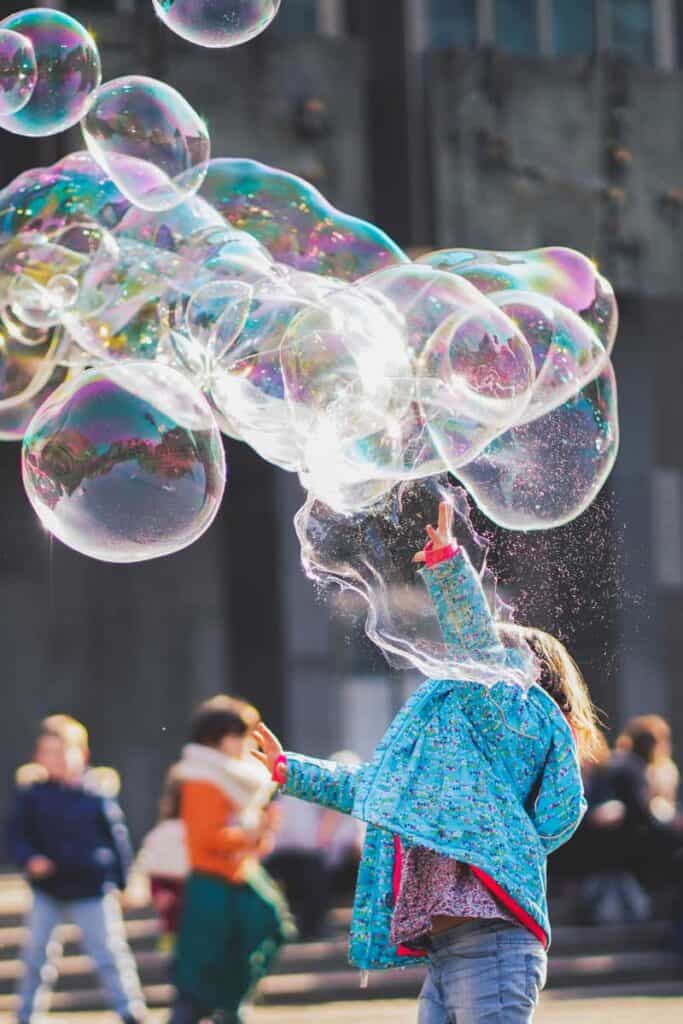 girl playing with giant bubbles refracting light art